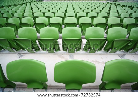 Rows of folded, green, plastic seats in very big, empty stadium. Focus on front seats
