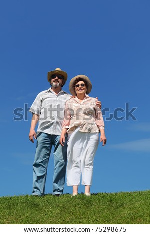 old man and woman in straw hats and sunglasses standing on summer lawn and embracing