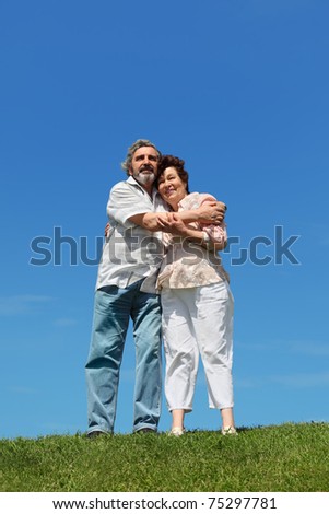 old man and woman standing on summer lawn, embracing and smiling