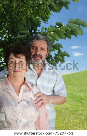 old man embracing old woman from back, summer tree