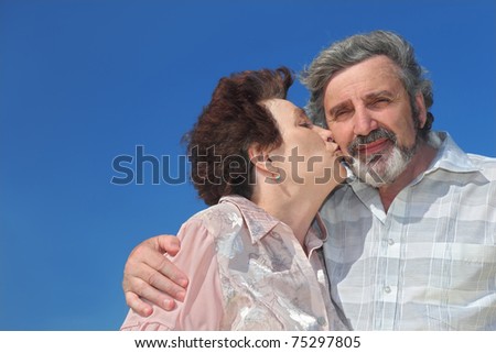 portrait of old woman kissing man cheek, blue sky
