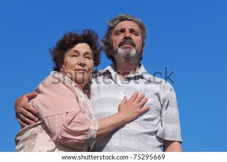 old woman and man standing and embracing, blue sky