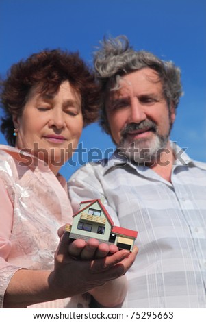 old man and woman holding little model of house, blue sky, focus on house