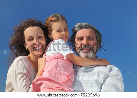family with girl, mother and grandfather smiling and embracing, blue sky