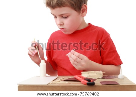 little boy in red T-shirt crafts at small table, boxcutter, glue