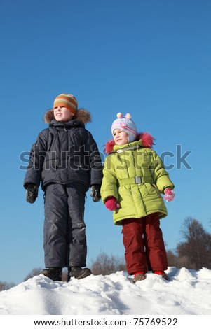 little girl in green jacket and boy standing at snow outdoors at winter and looking away