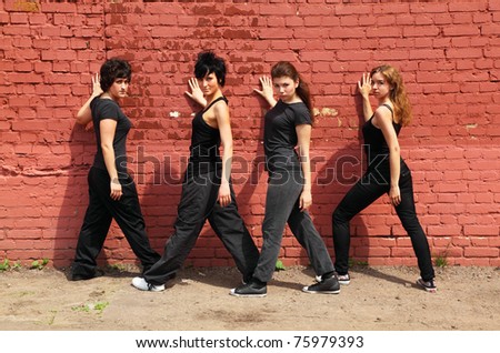 Four girls in same black clothes standing back and turning body on background of brick wall