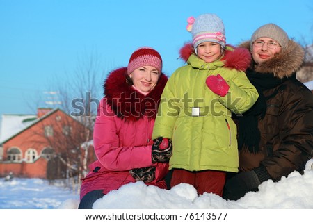 father, mother and daughter standing outdoors in winter near house, mother holding daughter hand