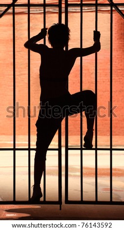 Silhouette of dancing girl in the dark, she climbing on latice with raised leg