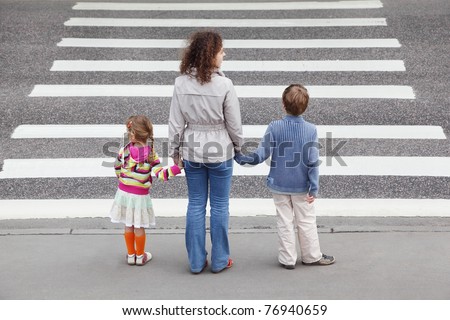 young mother holds hand of his little daughter and son and standing near cross road, behind