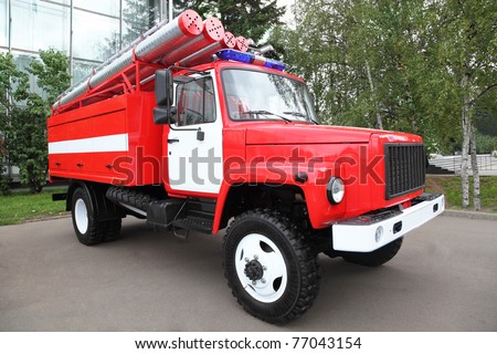 Big red fire engine with pipes and flasher on the roof at summer day