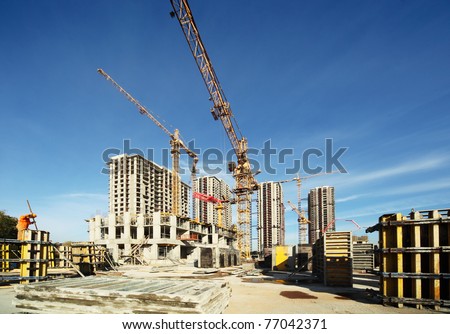Working tall cranes inside place for with tall buildings under construction under a blue sky