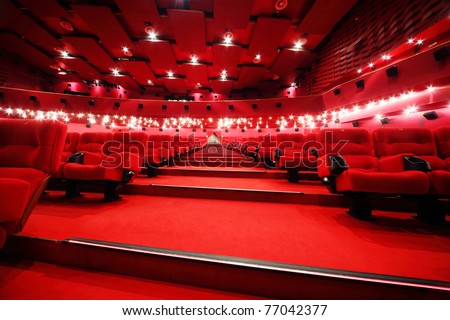 Low-angle view of stairs between rows of comfortable red chairs in illuminate red room cinema