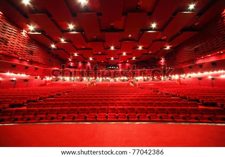 View from stage on ceiling and rows of comfortable red chairs in illuminate red room cinema
