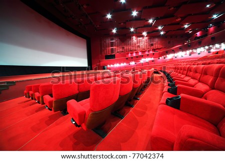 View from stairs on rows of comfortable red chairs in illuminate red room cinema