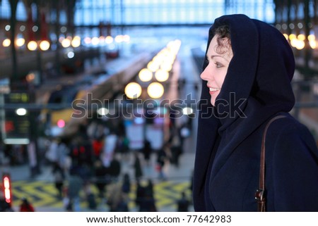 Young smiling woman close up stands in profile on the second floor of the train station on the background of the trains. Background with shallow depth of focus.
