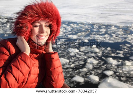 beautiful young woman in red jacket, smiling and standing near river at winter