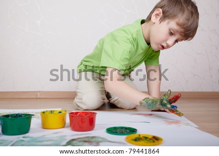 Boy in the green t-shirt draws color paints with his fingers on the sheet of paper