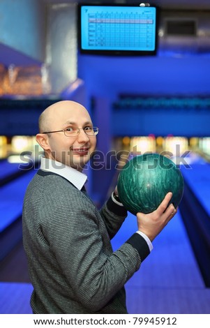 Man in glasses stands sideways and holds  ball for bowling