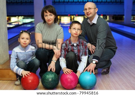 Family from four persons  of squatting in club for bowling and holds on to balls, focus on children and balls