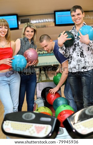 Two girls and two youths stand near tenpin bowling with balls for playing bowling and smile, focus on girl and fellow on sides