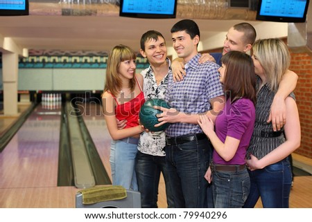 One fellow holds ball for bowling and his friends stand alongside with him and all look at him, focus on  man in center.