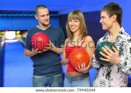 Two men holds  balls for bowling and look at girl in center, focus on youth on left and girl in center