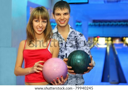Fellow and girl stand alongside with balls for bowling during rest in club, focus on girl