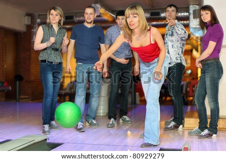 Girl throw ball on lane for bowling and friends worry for result, focus on girl in center