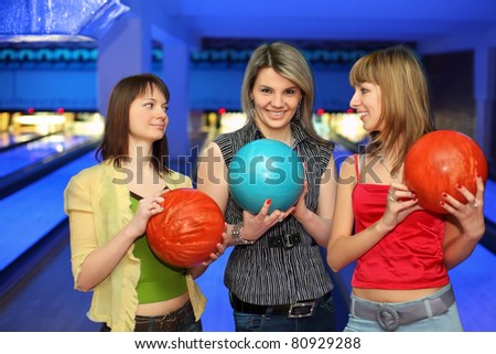 Three girlfriends hold balls for bowling and look on each other, focus on  girl in center