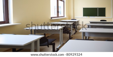 Empty beige classroom with wooden school desks and simple black chairs, view from desk on school board