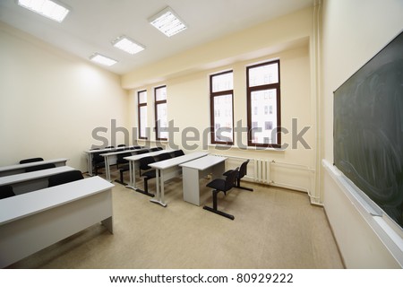 Empty beige classroom with wooden school desks, simple black chairs and green school board