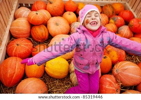 Little girl with drawing on cheek in big box with pumpkins
