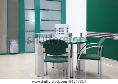 Table and some chairs in clean, simple and empty office with green decoration; focus on chair