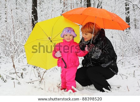 Grandmother and granddaughter with yellow and orange umbrella stand in woods in snow at winter