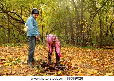 little brother and sister in autumn park poke sticks in old rusty hatch