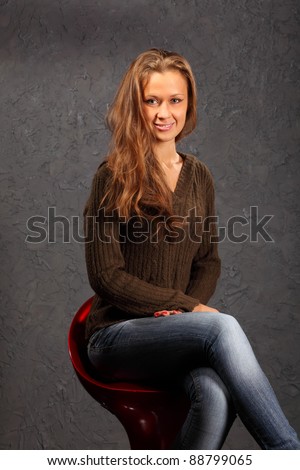 beautiful smiling girl wearing blouse and jeans sits on red chair in studio