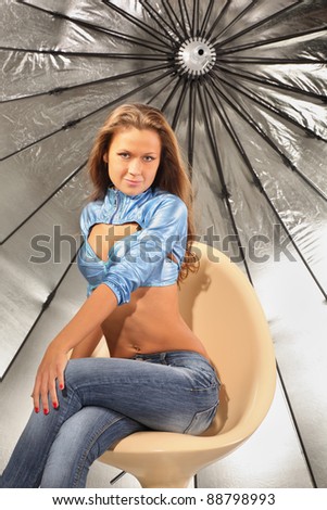beautiful girl wearing jeans sits on chair near big silver umbrella in studio
