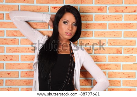 beautiful elegant brunette woman stands near brick wall and looks mysteriously