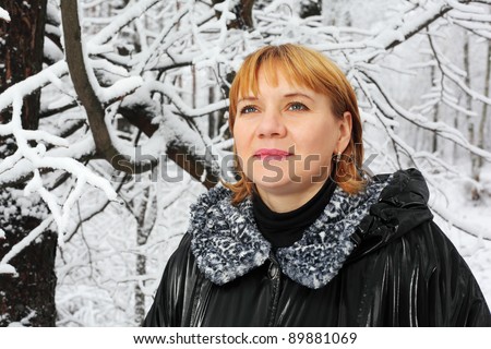Red-headed woman dressed black jacket look up in woods in snow at winter