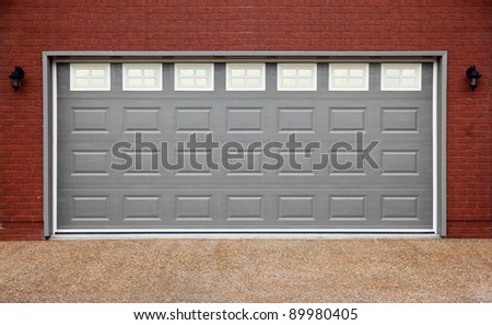 Big garage with gray doors, brick wall and asphalt driveway
