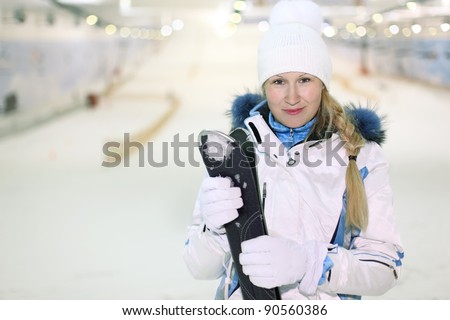 Young blonde smiling woman dressed in white sports clothes stands and keeps skis in indoor ski