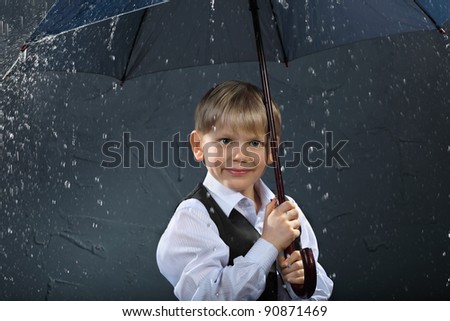 smiling boy dressed in white shirt and black vest standing under umbrella in rain