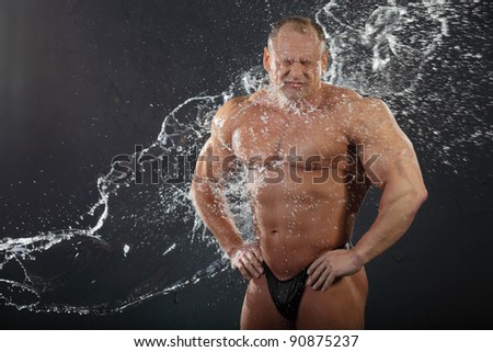 Water flows on undressed tanned bodybuilder with wrinkled face.