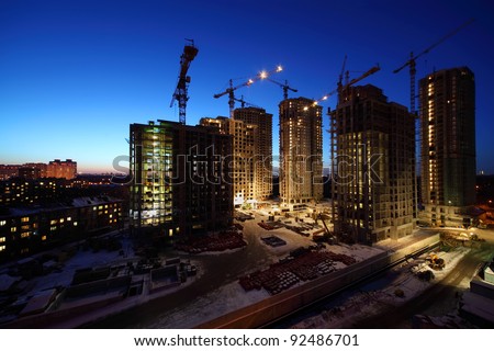 Seven high buildings under construction with cranes and illumination at night