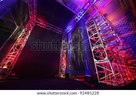 Colorful illuminated way with grid to boxing ring inside fight club; many lights