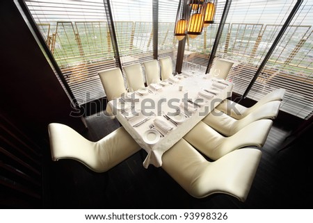 table with white tablecloth and serving and ten white chairs in empty lit restaurant