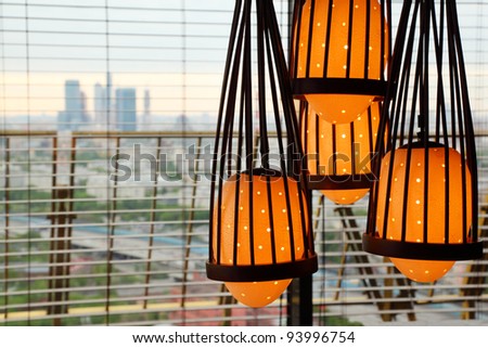 Yellow lamp hanging from ceiling, outside window skyscrapers of city
