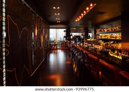 bar counter with red tall chairs in empty comfortable restaurant; lot of drinks on shelves