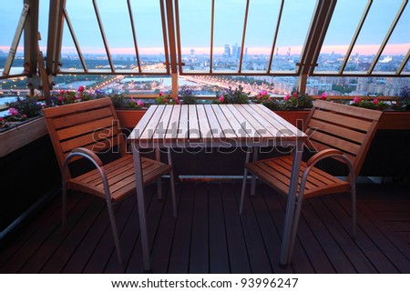 Wooden chairs and table at terrace in empty restaurant; panorama of evening Moscow